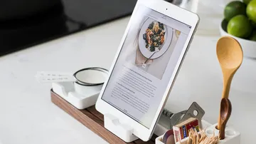 Tablet stands on stand, shows recipe in a kitchen.