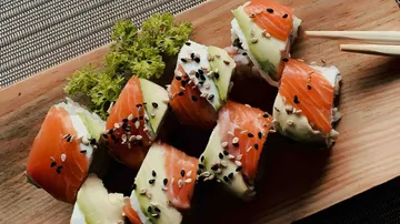 Sushi rolls lie on a wooden board, surrounded by fresh vegetables.