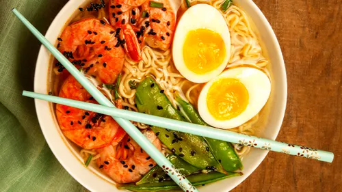 Bowl of noodles, prawns and eggs, next to chopsticks.
