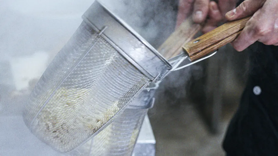 A colander lifts cooked food over steaming water.