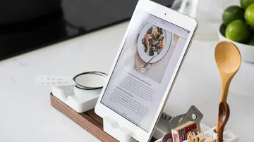Tablet shows a recipe surrounded by kitchen appliances and ingredients.