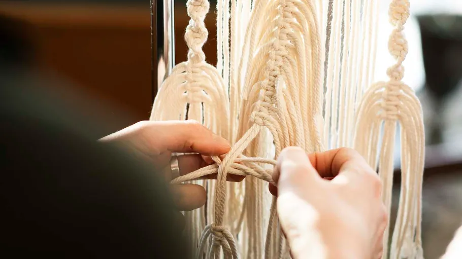 Hände knoten helle Schnüre zu einem Wandbehang, kreativ.