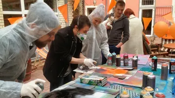 Groups of people spray paint onto outdoor canvases.