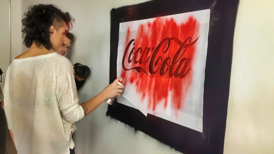 Frau sprüht rote Farbe auf Coca-Cola-Logo im Hintergrund.