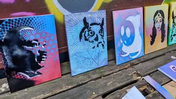 Spray-painted canvases on wooden surface outdoors.