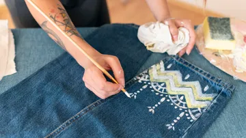 A hand paints patterns on jeans.