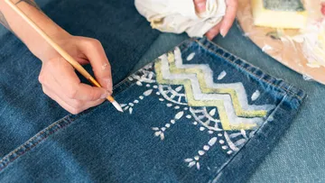 A hand paints patterns on jeans.