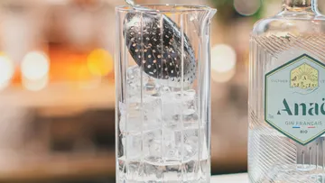 Glas mit Eiswürfeln, Sieb über dem Glas, Barhintergrund.