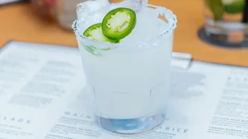 Kalter Cocktail mit Limetten und Jalapeños auf Tisch.
