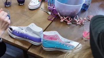 Bunte Schuhe werden auf einem Tisch bemalt, umgeben von Getränken.