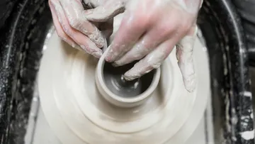 Hands form a clay cup on a turntable.
