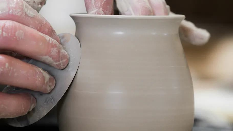 Hands form a ceramic vase with a tool edge.