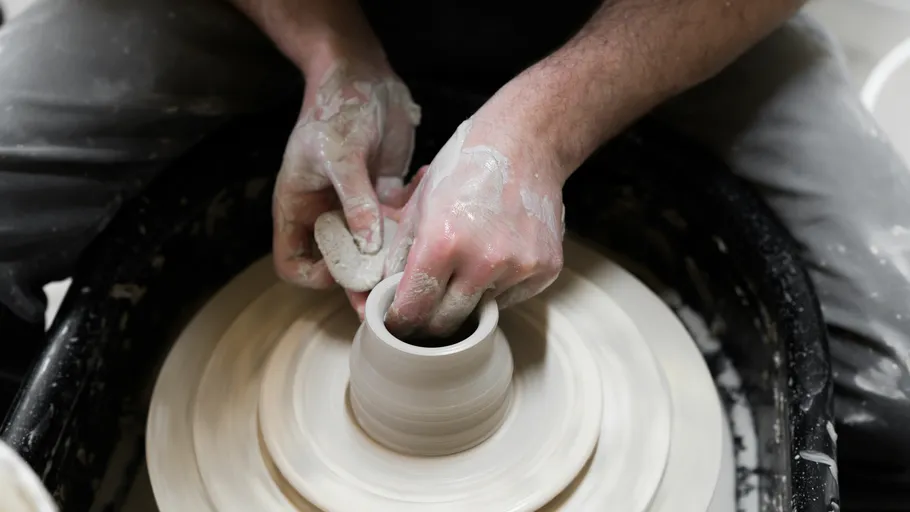 Hands form a clay container on the potter's wheel.