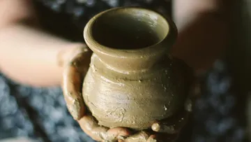 The clay pot is held by hands in a creative environment.