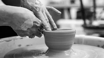 Hands form a clay pot on a turntable.