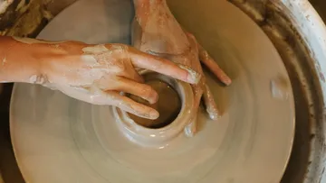 Hands form clay on a potter's wheel.