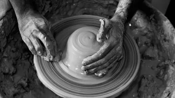 Potter hands form a lump of clay on the lathe.