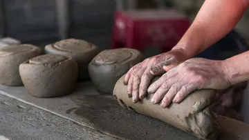 Hands form pieces of moist clay on a workbench.