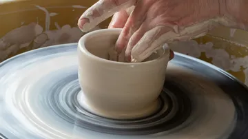 Töpferscheibe dreht sich, Hände formen einen Tonbecher.