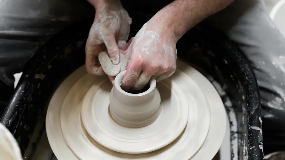 A potter shapes a cup on a potter's wheel.