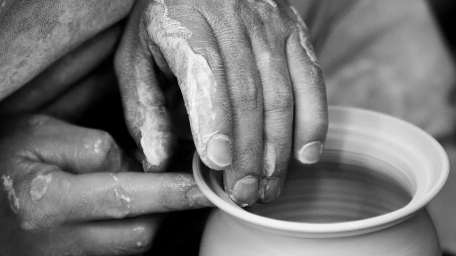 Hands form a cup out of moist clay on a turntable.