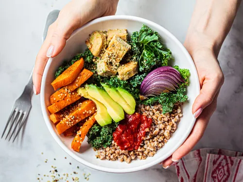 Eine Schüssel mit Gemüse, Hühnchen und Quinoa wird gehalten.