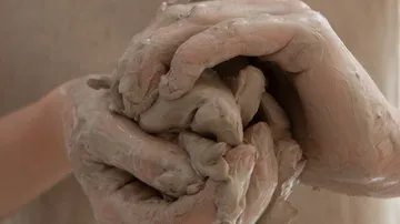 Hands form and process moist clay in a studio.