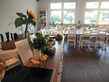 Küche mit frischen Zutaten, Tischen für Gäste im Hintergrund.