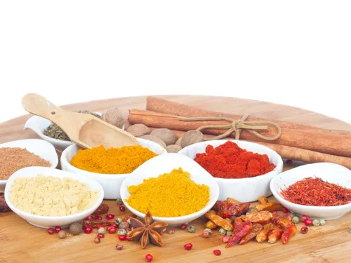 Colourful spices arranged in bowls on a wooden plate.