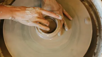 Hände formen Ton auf einer Drehmaschine in einem Atelier.