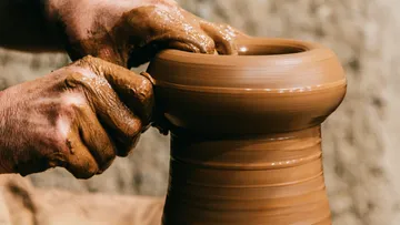Potter shapes a clay cup on a turntable with hands.