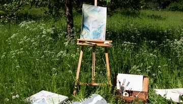 Easel with a painting stands in green grass.