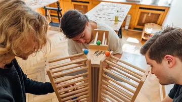 Drei Personen bauen gemeinsam ein Holzspielzeug auf.