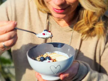 A person eats yogurt from an outdoor bowl.