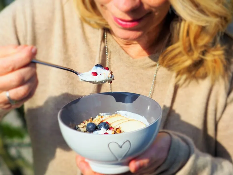 Eine Person isst Joghurt aus einer Schüssel im Freien.