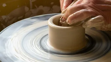 A hand forms a clay pot on a potter's wheel.