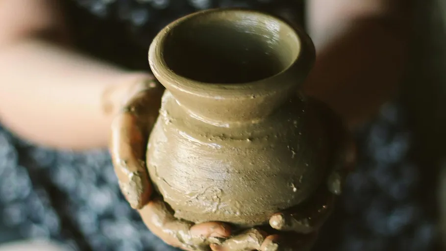 Clay jug is held by hands, background blurred and creative.