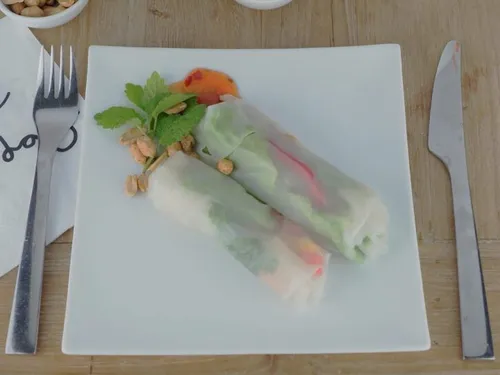 Reispapierrollen liegen auf einem Teller mit Kräutern.