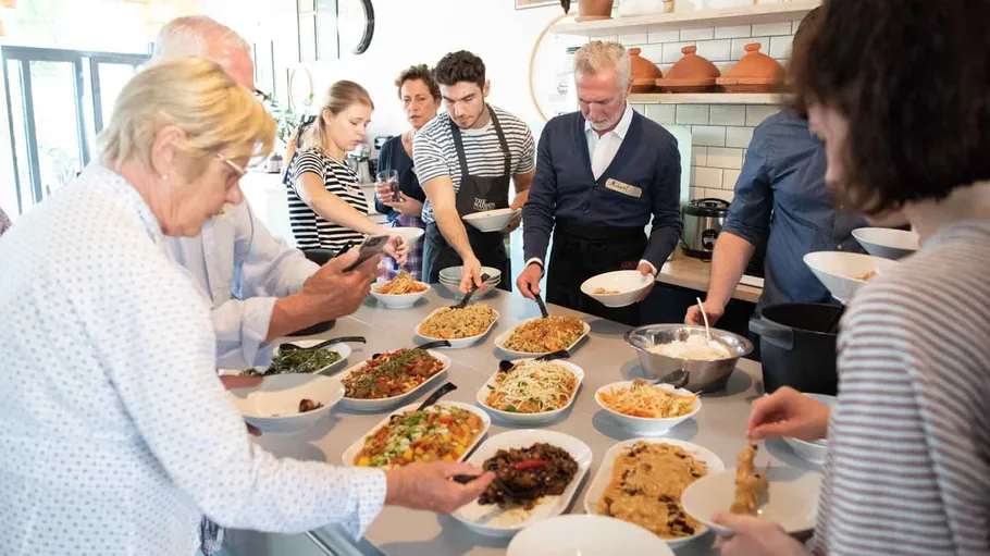 People serve food from a table in a kitchen.
