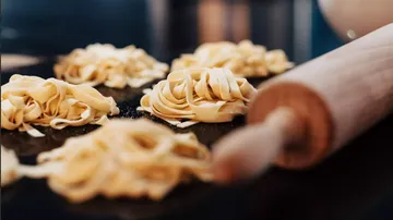 Fresh pasta is lying on a surface next to a rolling pin.