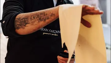 One hand holds a strip of dough in a kitchen.