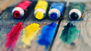 Tubes of paint lie on wood, paints have been pressed along the tubes.