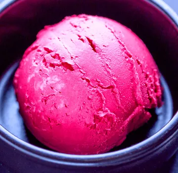 Rote Eiskugel liegt in schwarzer Schüssel.