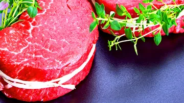 Rotes Fleisch mit Kräutern auf schwarzem Untergrund arrangiert.