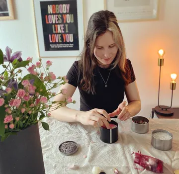Woman mixes materials in black container surrounded by flowers.