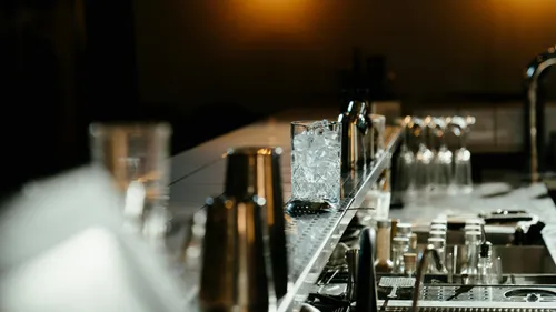 Glas mit Eis steht auf einer Bar, umgeben von Gläsern.