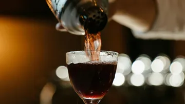 Ein Cocktail wird aus einem Shaker in ein Glas gegossen.