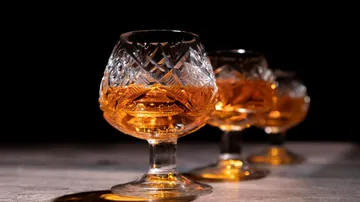 Crystal glasses with amber-colored drink are on a table.