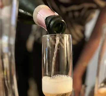 Sektflasche gießt Schaumwein in ein Glas bei Feier.