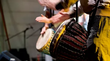 Drums are played on a stage by people.